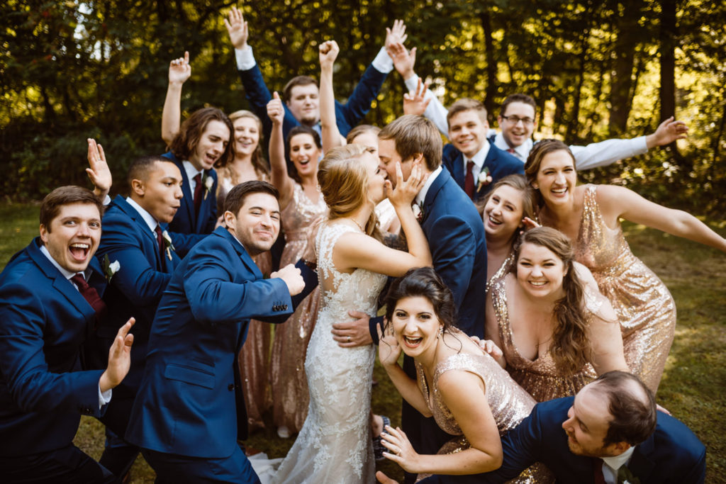 wedding party portrait of friends cheering for bride and groom kissing