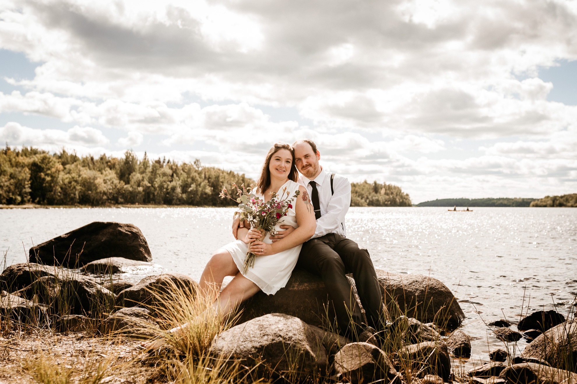 wedding couple sitting on rocks on lakeshore