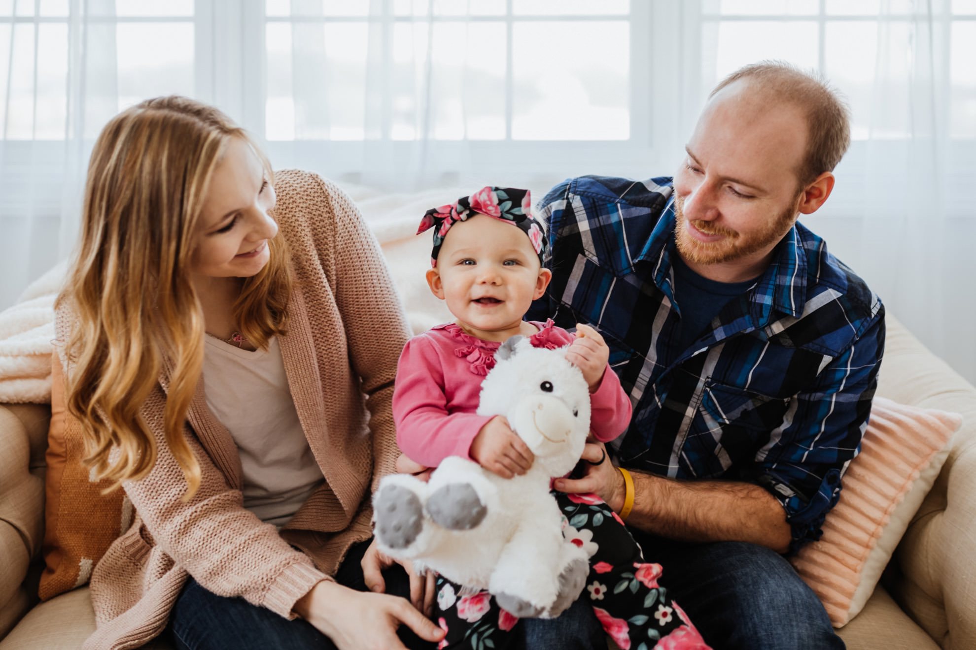 parents smiling at one year old girl on couch