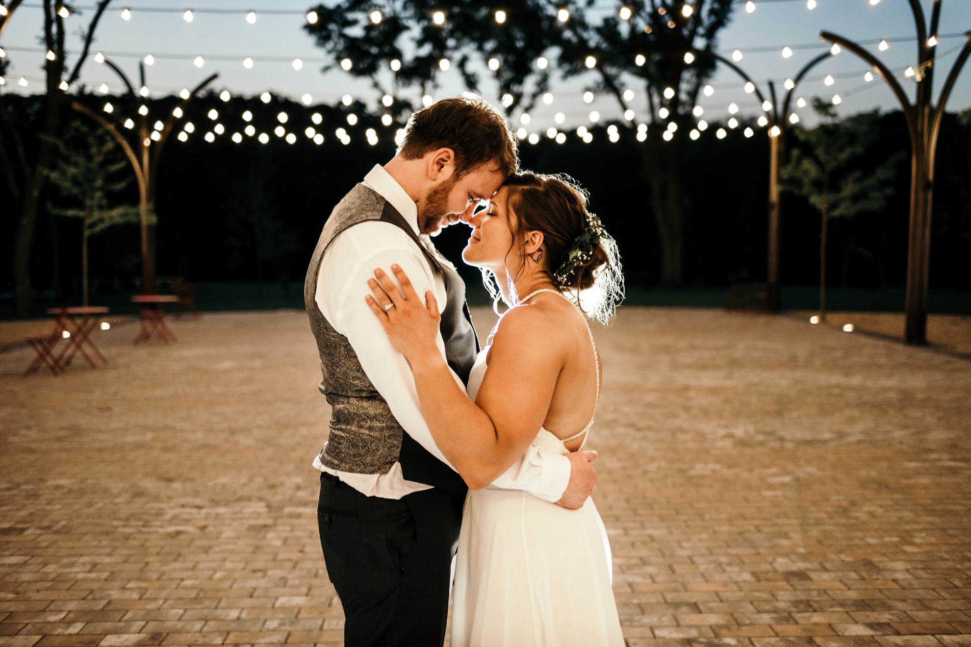 bride and groom cuddling under string lights outside