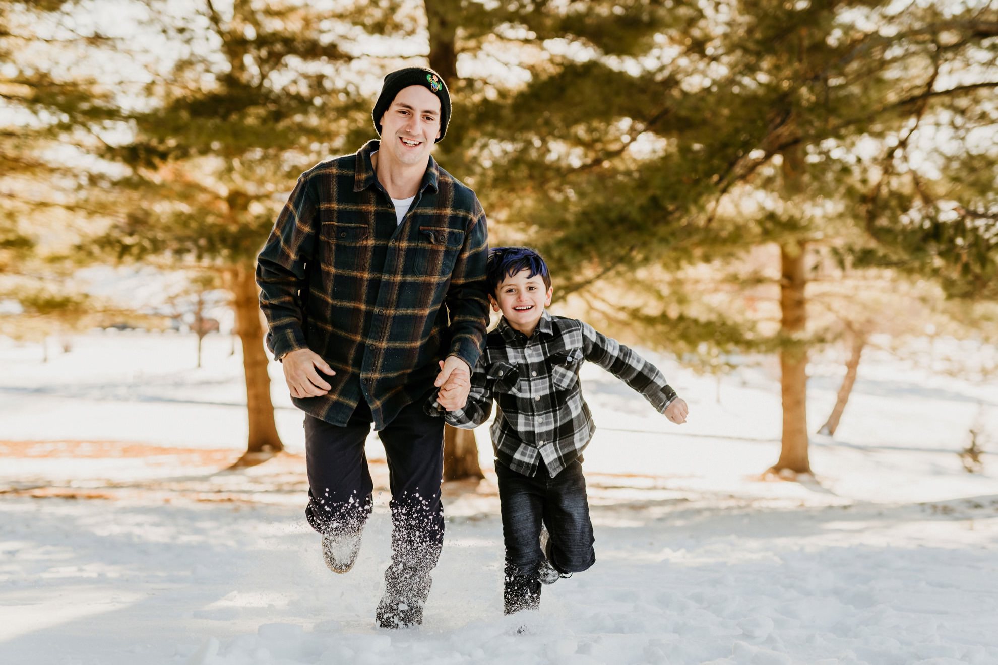 father and son smiling and running through the snow holding hands towards camera