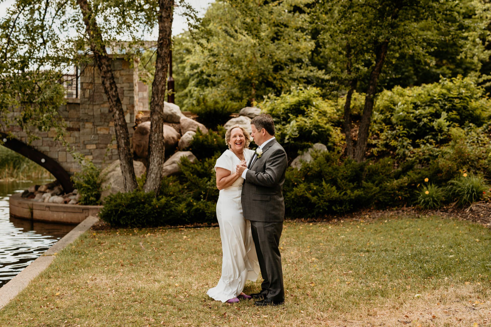 bride and groom dancing and laughing together in beautiful nature park in summer