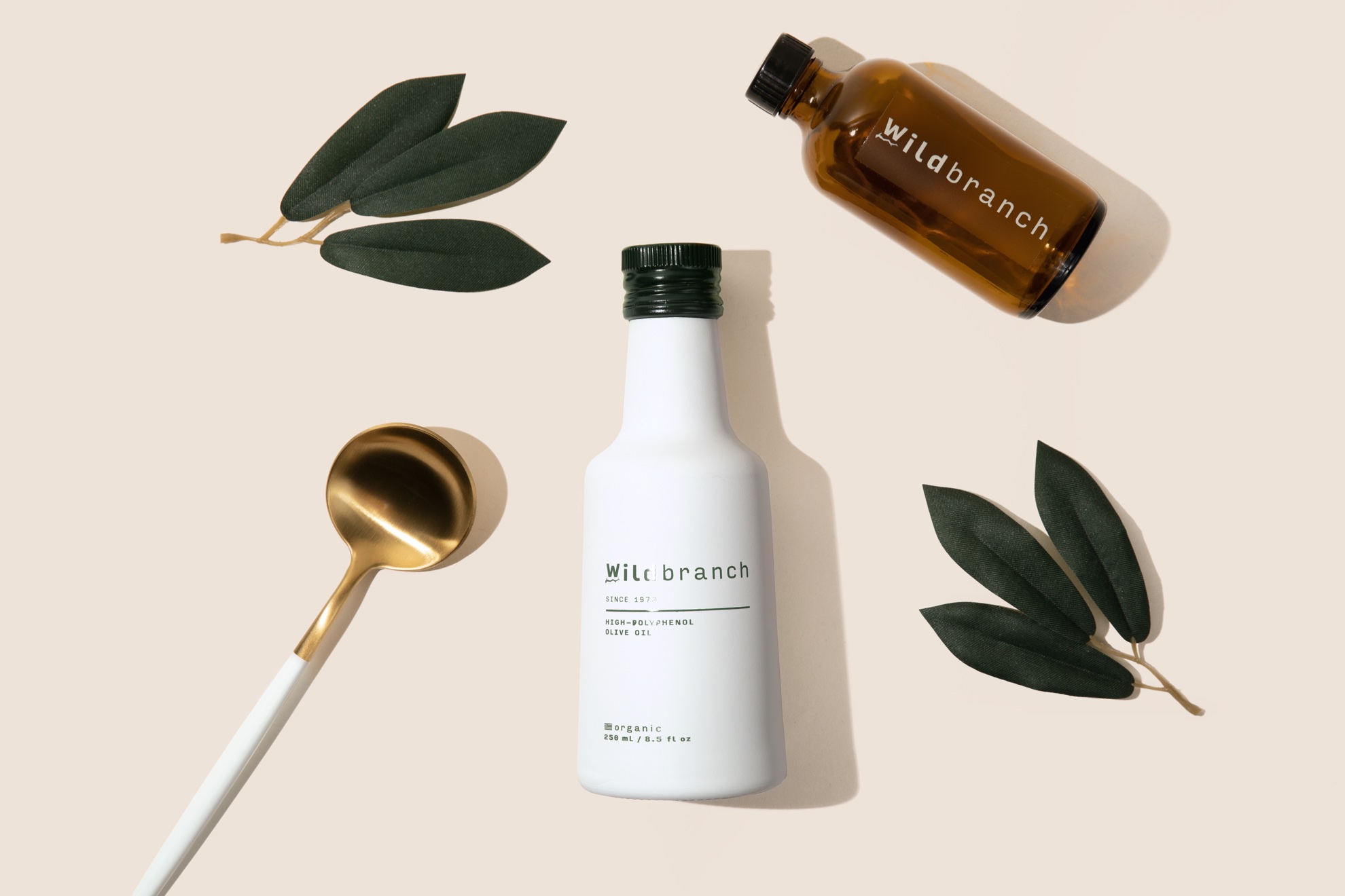 flatlay photo of olive oil bottle with olive leaves and spoon