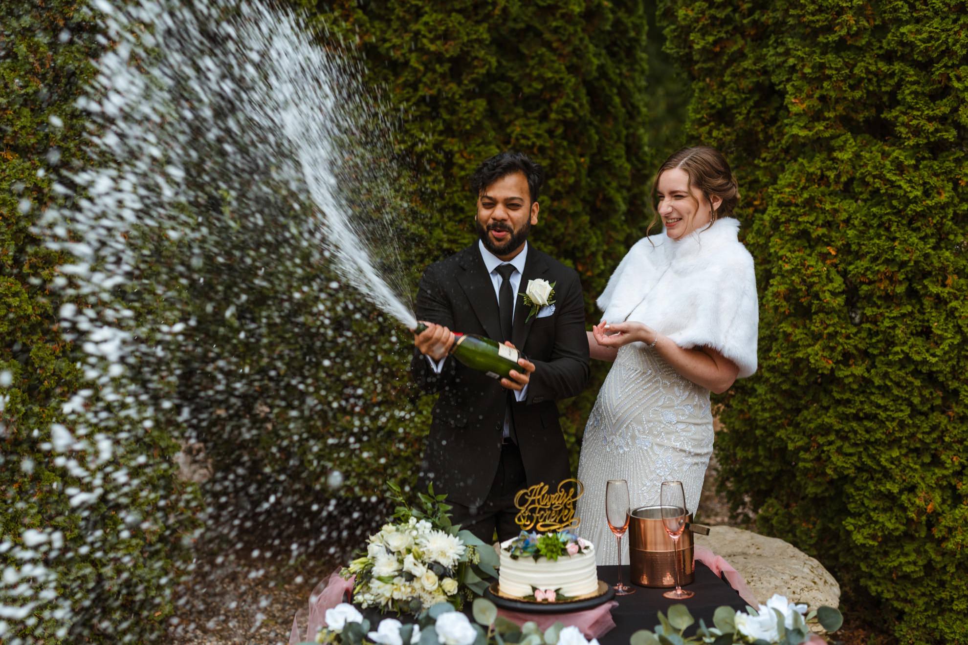 bride and groom popping a bottle of champagne after eloping in a city park garden